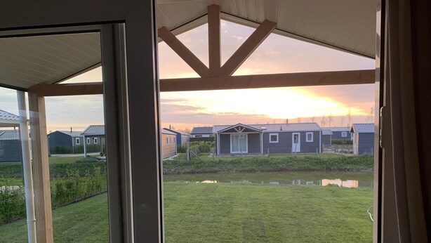En utsikt från ett takförsett utomhusområde med ett trädäck, en gräsyta och en liten damm.