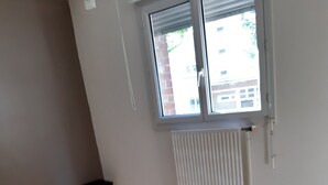 Una habitación con un ventanal grande, un radiador blanco y suelo marrón.
