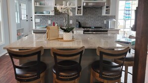 A modern kitchen with a large island, bar stools, and a backsplash of gray tiles.