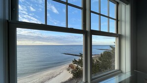 A view from a window overlooking a beach with a rocky outcrop and a wooden fence. - Cape Cod Oceanfront New Condo with Ocean View & Private Beach, OceanBeachVista! (Dennis)