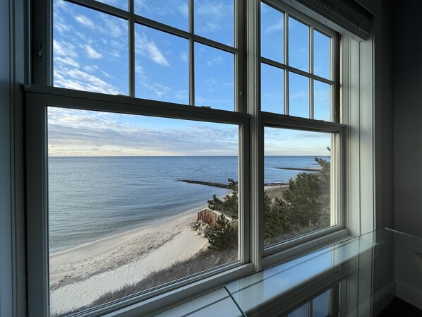 A view from a window overlooking a beach with a rocky outcrop and a wooden fence.