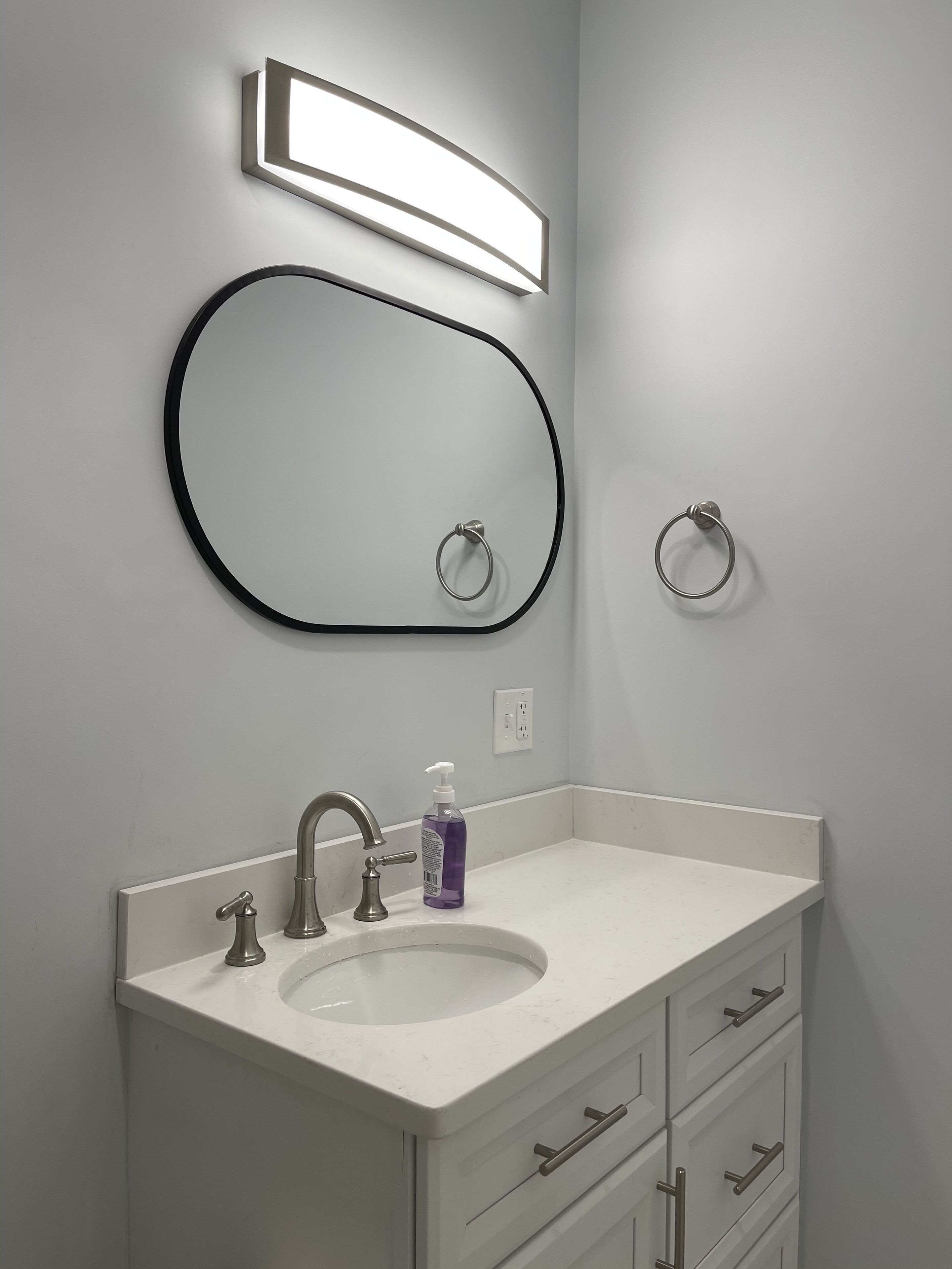 A bathroom with a white sink, a mirror with a black frame, a soap dispenser, and a towel ring.
