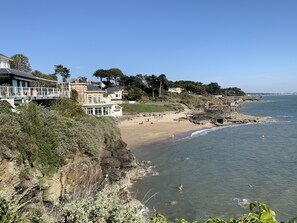 Ein Küsteneigentum mit Strand, felsigen Klippen und einem großen Haus mit zahlreichen Fenstern und Balkonen mit Meerblick.