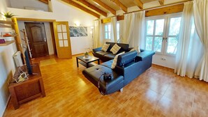 Un'ampia zona giorno con soffitto in legno, divano blu, tavolino da caffè e una porta che dà su un'altra stanza.