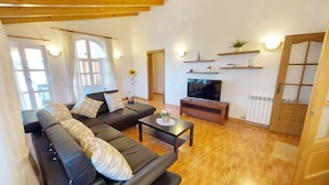 Un soggiorno con un divano nero, un tavolino da caffè e una TV su un mobile in legno. Si notano travi in legno al soffitto, una porta con pannelli di vetro e un termosifone sulla parete.
