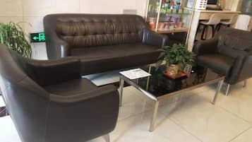 A lobby with a brown leather sofa, a glass coffee table, and a small plant.