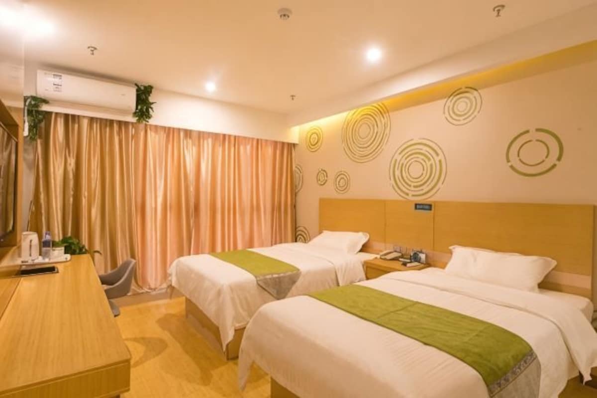 Habitación de hotel con dos camas, un escritorio, una silla, un equipo de aire acondicionado y una cortina.
