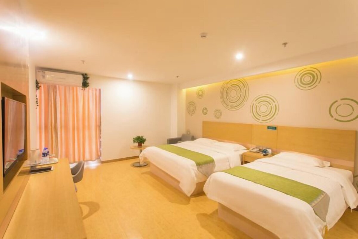 Habitación de hotel con dos camas, un escritorio, una silla, una mesita con una planta y una pared con diseños circulares.