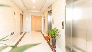 Un hall d’hôtel moderne avec un sol en marbre, une plante en pot et un ascenseur métallique.