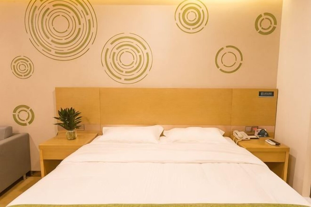 Habitación de hotel con una cama, una mesita de noche con teléfono, una lámpara y una planta.