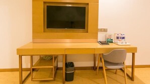 Een houten bureau met een televisie, een stoel, een prullenbak en een klein tafeltje met een waterfles en zakdoekjes.