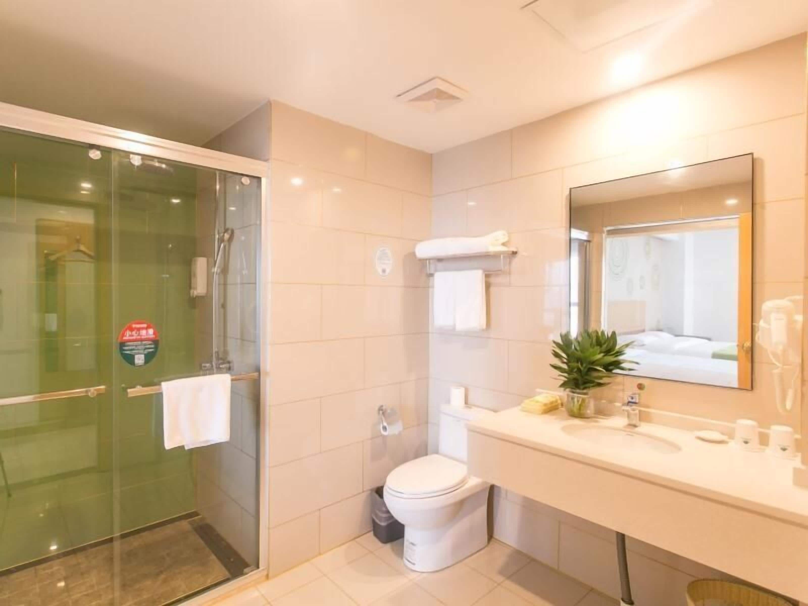 Un baño moderno con cabina de ducha de vidrio, inodoro, lavabo con espejo y una pequeña planta en maceta.