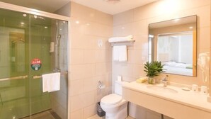 Een moderne badkamer met een glazen douchecabine, toilet, wastafel met spiegel en een kleine potplant.