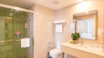 Un baño moderno con cabina de ducha de vidrio, inodoro, lavabo con espejo y una pequeña planta en maceta.