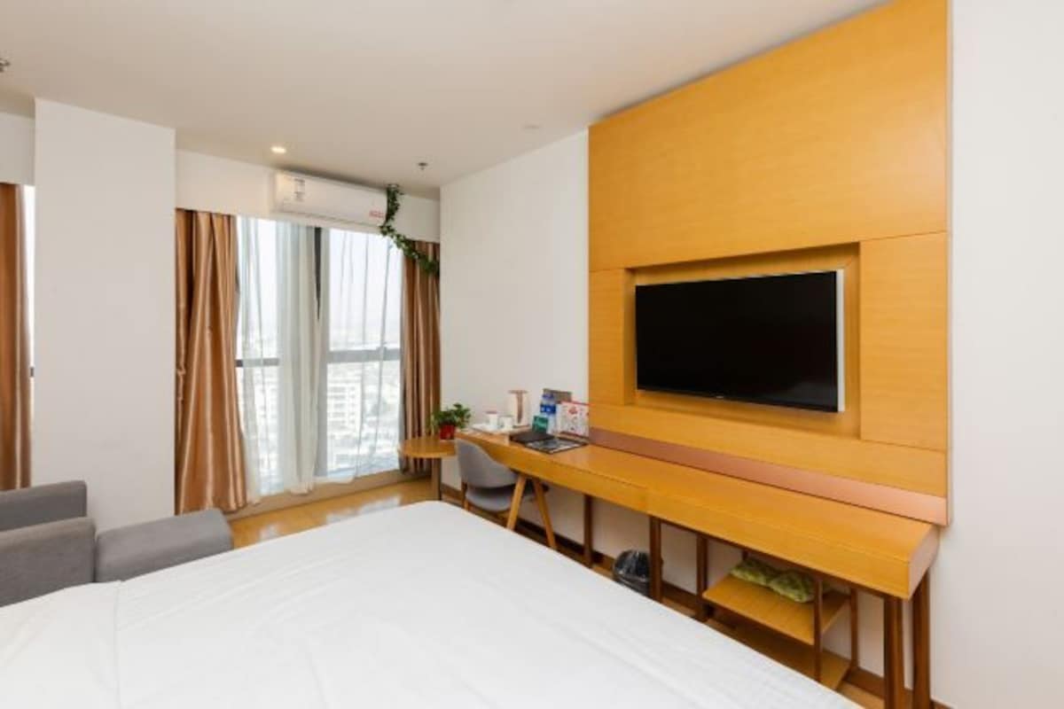 Habitación de hotel con cama, escritorio, silla, televisor y ventana con cortinas.