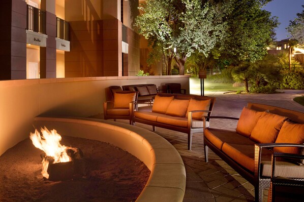 An outdoor seating area with a fire feature, surrounded by a building with balconies and a tree.