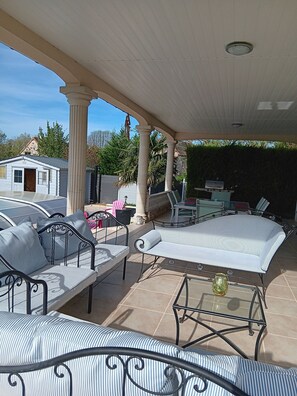 Eine Terrasse im Freien mit überdachter Sitzecke, inklusive einer Couch und Sesseln sowie einem Tisch mit Glasplatte.