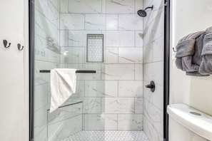 Eine gläserne Dusche mit weißen Marmorfliesen, einem Handtuchhalter und einem sechseckigen Fenster.
