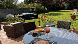 Un espacio exterior para comer con una mesa redonda, muebles de mimbre y una parrilla al fondo.