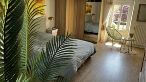 Un dormitorio con cama, mesita de noche, lámpara, silla, ventana y planta.