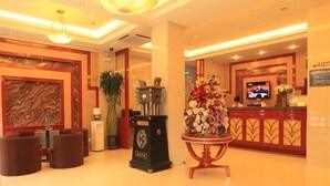 A hotel lobby with a reception desk, a large floral arrangement, a clock, and a green tree emblem on the floor. - Greentree Inn Lanzhou Yantan Road Express Hotel (Lanzhou)
