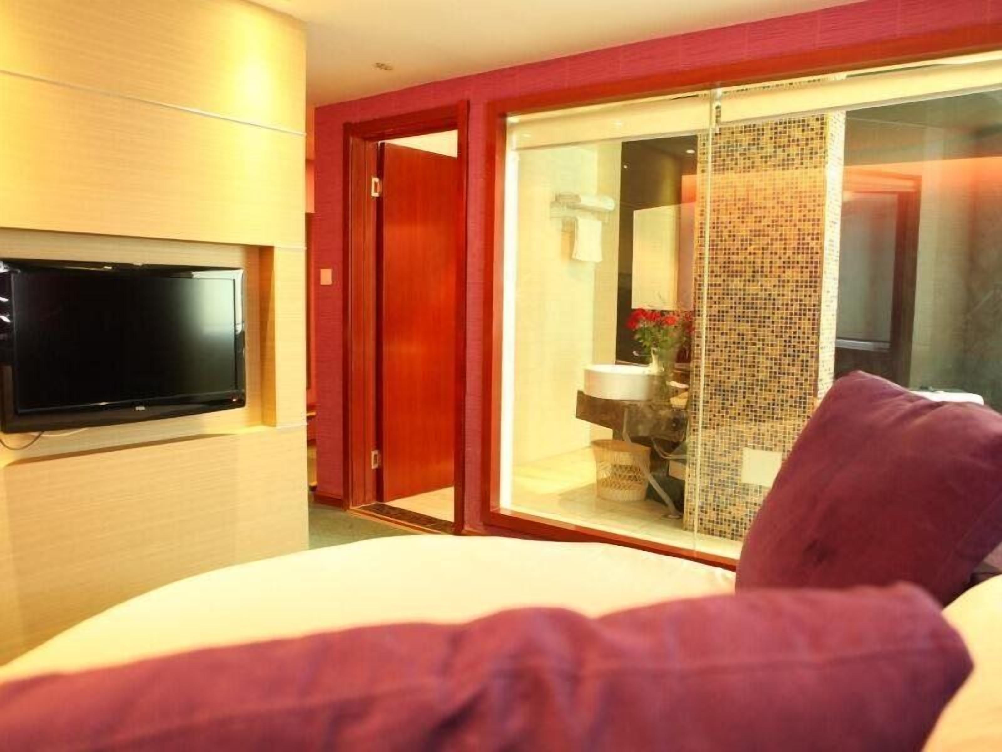 A hotel room with a bed, a television mounted on the wall, a sliding glass door leading to a bathroom, and a red door.