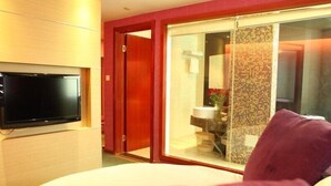 A hotel room with a bed, a television mounted on the wall, a sliding glass door leading to a bathroom, and a red door. - Greentree Inn Lanzhou Yantan Road Express Hotel (Lanzhou)