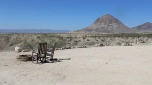 Paisaje desértico con una montaña al fondo y una silla de madera en primer plano.
