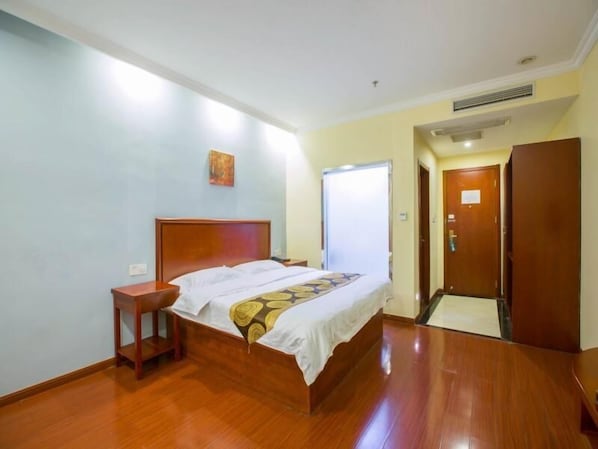 A hotel room with a wooden bed, a nightstand, a door, and a wall with a painting.