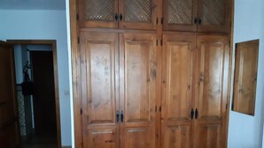 A room with a large wooden wardrobe, a blue chair, and a door leading to another room. - Casa Alba E Irene (Bubión)