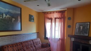 A living room with a patterned sofa, a fireplace, and a large painting on the wall. - Casa Alba E Irene (Bubión)