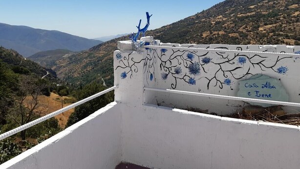 A balcony with a white railing, decorated with blue floral patterns and a blue sculpture. The background features a mountainous landscape. - Casa Alba E Irene (Bubión)