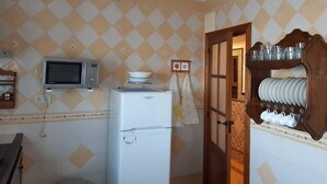 A compact kitchen with a microwave, refrigerator, and a wooden cabinet with dishes. - Casa Alba E Irene (Bubión)