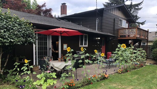 A patio area with a table and chairs, a red umbrella, and a variety of potted plants and flowers. - Emerald City Cozy Studio Suite - Stay near university fun – 5 min drive (Eugene)