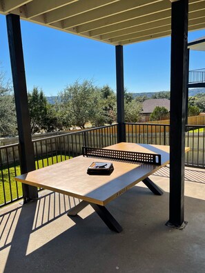 An outdoor patio with a table and chairs, surrounded by a metal railing, overlooking a residential area with trees and houses.