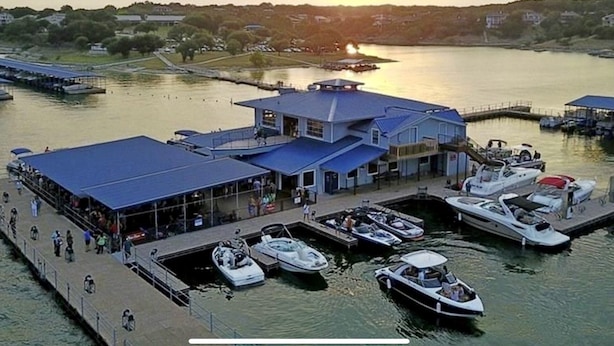 Een jachthaven met aangemeerde boten, een overdekt gebied met mensen en een gebouw met een blauw dak.