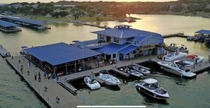 A marina with boats docked, a covered area with people, and a building with a blue roof. - Panoramic Lake Travis View in Lago Vista (Lago Vista)