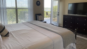 Een slaapkamer met een groot bed, een televisie op een dressoir en een balkon met uitzicht.