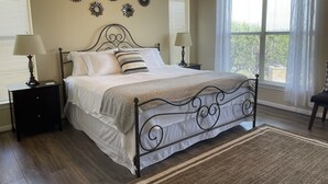 Een slaapkamer met een metalen bedframe, witte beddengoed, twee nachtkastjes met lampen en een groot raam met jaloezieën.