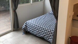 A bedroom with a bed, a window, and a red trash bin. - Studio Atypique (Fréjus)