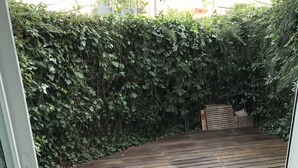 A wooden deck with a metal railing, surrounded by dense greenery. - Studio Atypique (Fréjus)
