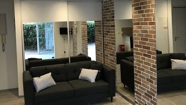 A modern living room with a black sofa, a large mirror, and a brick accent wall. - Studio Atypique (Fréjus)