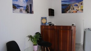 A reception area with a wooden desk, a black chair, a potted plant, and two framed pictures of coastal scenes. - Spiridoula villa (Santorini)