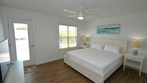 A bedroom with a bed, a ceiling fan, a window, a nightstand, a lamp, and a painting on the wall.