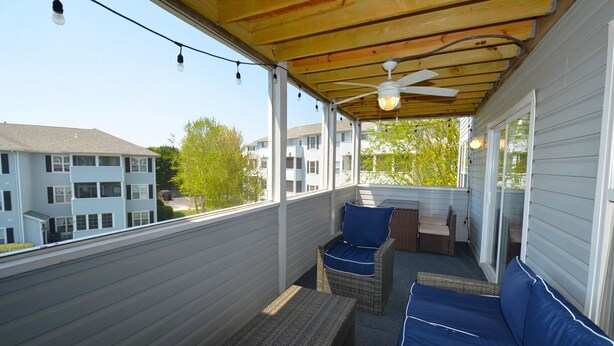 A covered balcony with wicker furniture, a ceiling fan, and string lights.