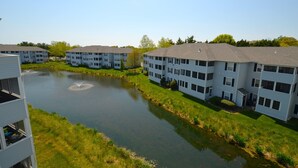 A residential building complex with a central water feature, likely a pond or small lake, surrounded by well-maintained lawns and trees.