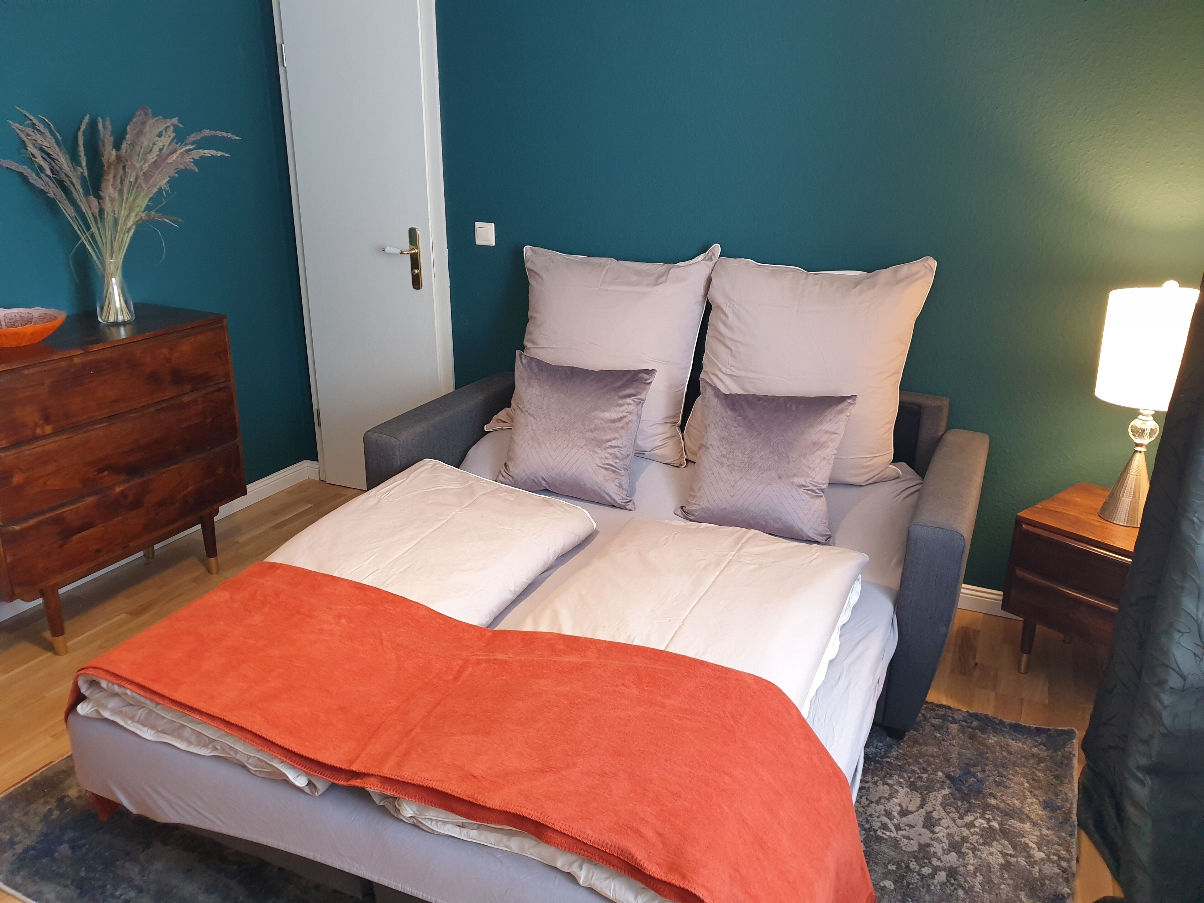 A bedroom with a bed, pillows, a dresser, a nightstand, and a lamp.