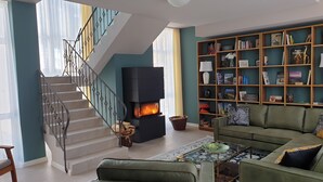 A living room with a staircase, a fireplace, a green sofa, and a bookshelf filled with books. - Vacation home for 12 people, 8 rooms, 4 bathrooms with fireplace and large lounge (Altenberg)