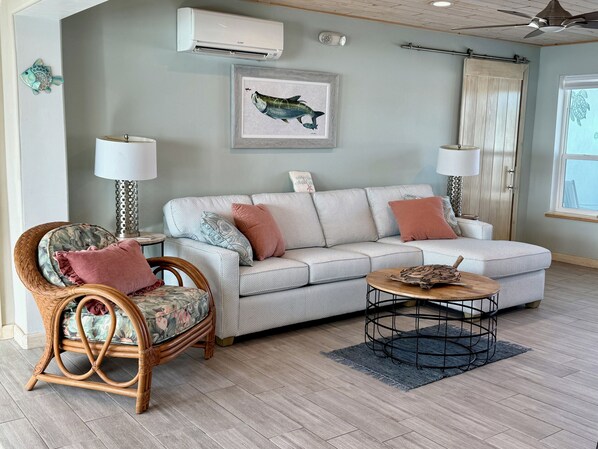 A living room with a wicker chair, a sofa, a coffee table, and a framed fish illustration on the wall. - Sea Salt Escape | Oceanfront Home with Pool & Dock | 3/3 (Marathon)