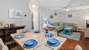 Un coin repas avec une table dressée pour quatre personnes, un canapé et un ventilateur de plafond.